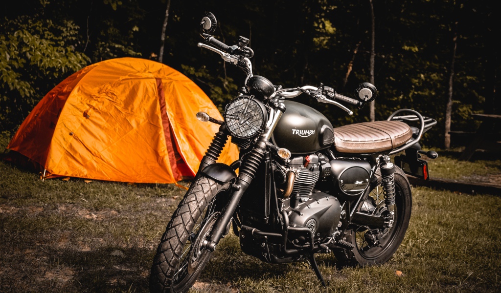 Черный мотоцикл Triumph на фоне оранжевой палатки