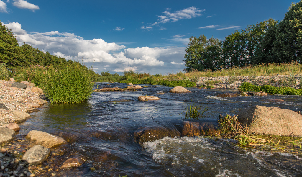 Быстрая речная вода стекает по камням под красивым голубым небом