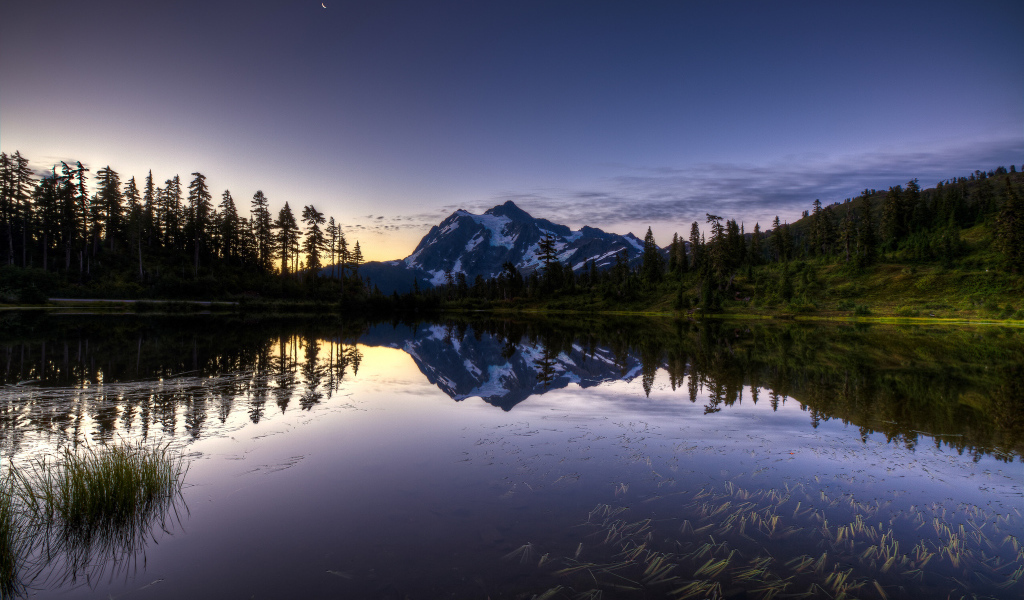 Заснеженная гора и лес отражается в озере вечером