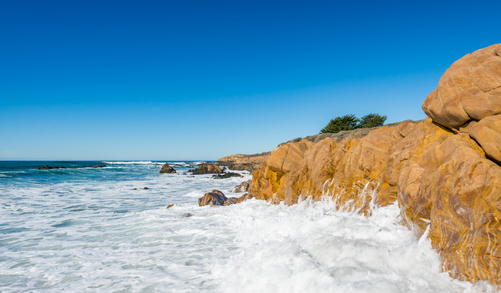 Белые волны бьются о скалы на берегу океана под голубым небом