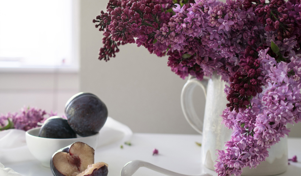 Красивый букет сирени в белой вазе на столе со сливами