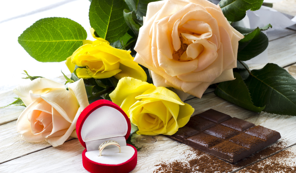 Букет роз на столе с шоколадкой и красной коробочкой с обручальным кольцом
