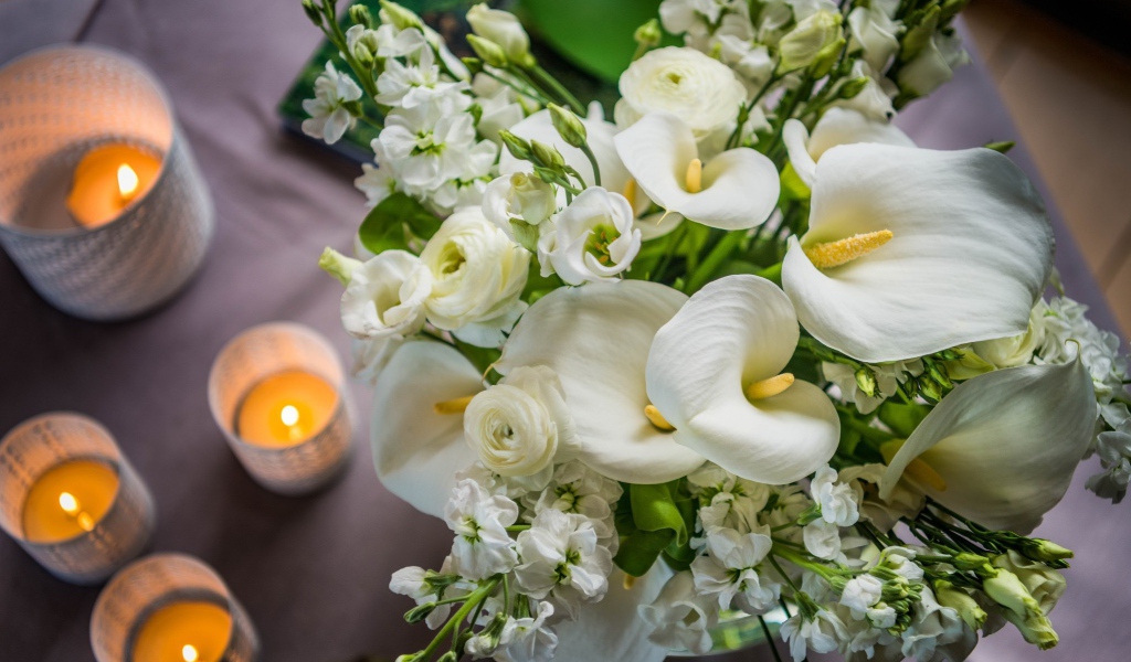 Букет белых цветов зантедеския и левкой с зажженными свечами на столе