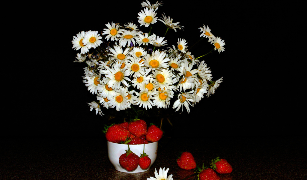 Белые полевые ромашки и клубника на столе на черном фоне