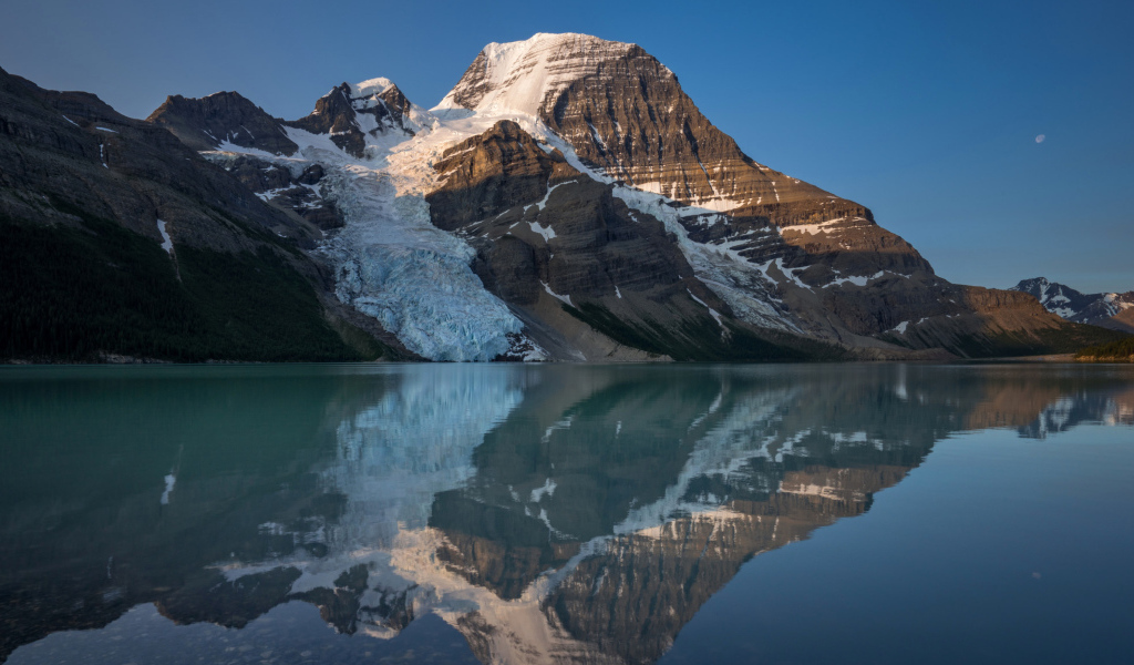 Гора в снегу отражается в водной глади озера 