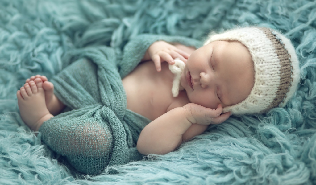 Грудной ребенок спит на зеленом меховом покрывале