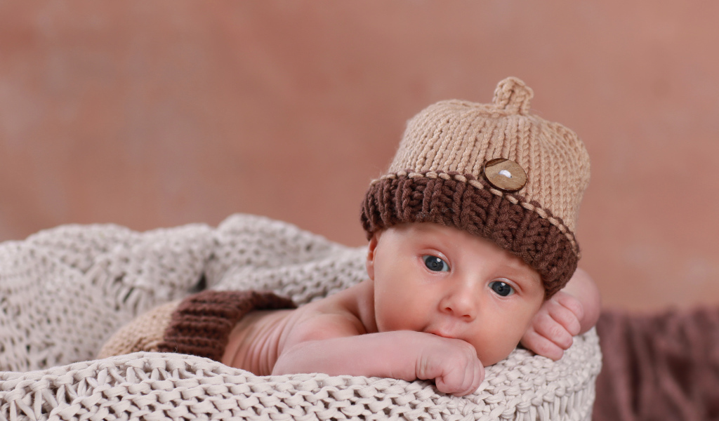 Грудной ребенок лежит в вязаной коричневой шапке