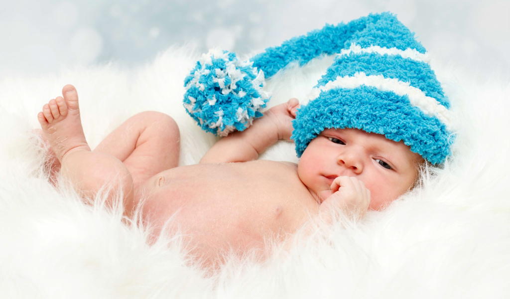 Грудной ребенок в голубой шапке с бубоном на голове
