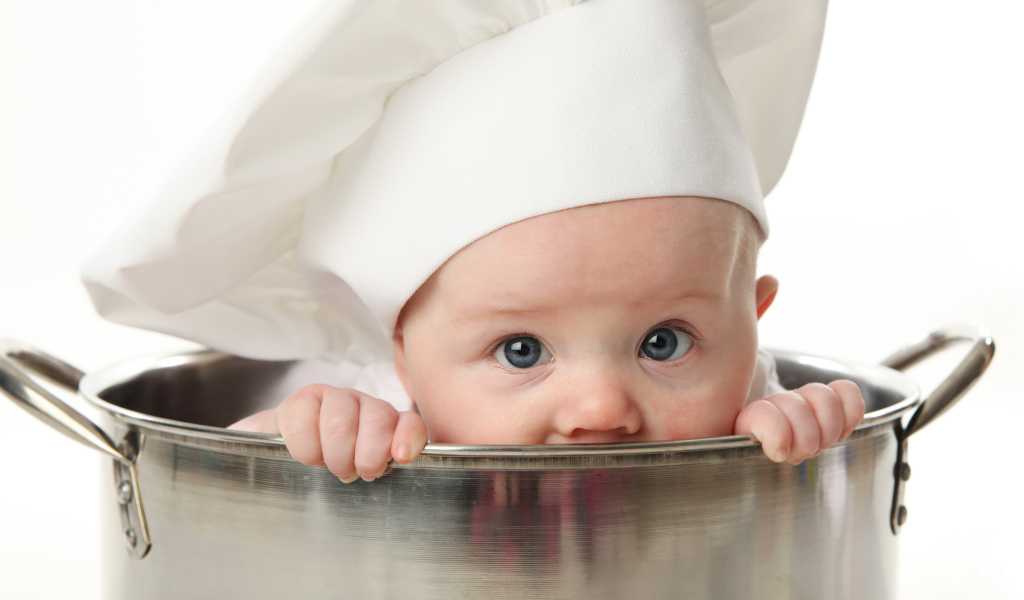 Грудной ребенок в шапке повара сидит в большой кастрюле