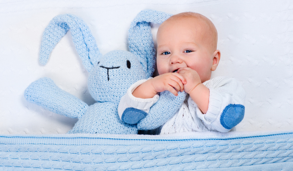 Милый младенец лежит в кроватке с голубым вязаным зайцем