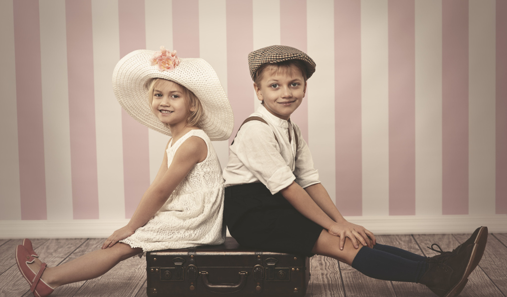 Девочка в большой белой шляпе и мальчик сидят на чемодане