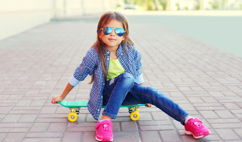 Девочка в солнечных очках сидит на скейтборде