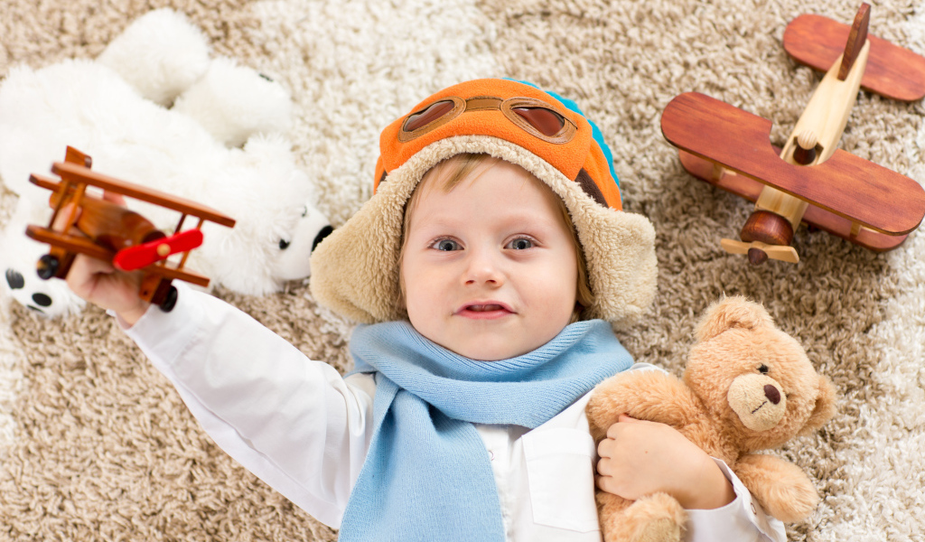 Маленький мальчик в шапке и игрушечным самолетом и медвежонком в руках