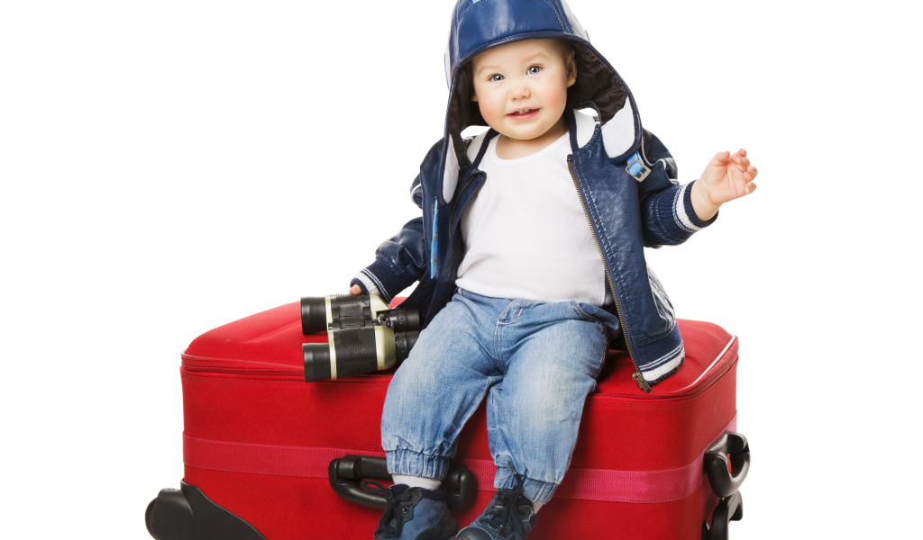 Маленький мальчик в шапке с биноклем сидит на красном чемодане