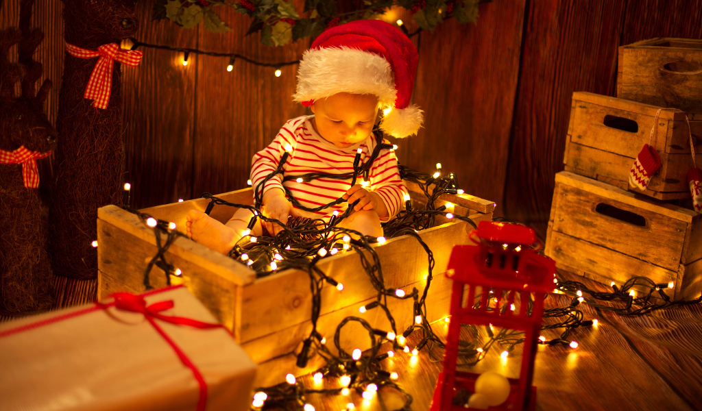 Маленький мальчик сидит в коробке с новогодней гирляндой