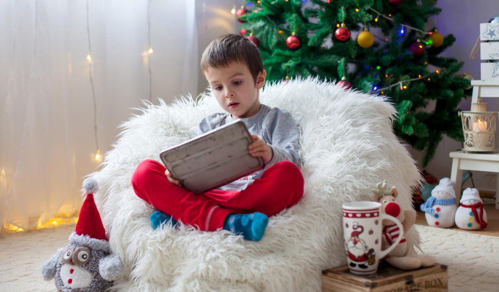 Маленький мальчик сидит в мягком кресле у новогодней елки