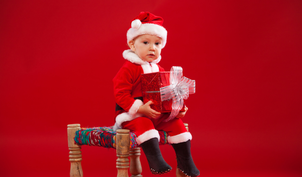 Маленький мальчик сидит на стуле с новогодним подарком