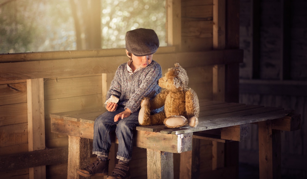Маленький мальчик сидит на деревянном столе с медвежонком Тедди