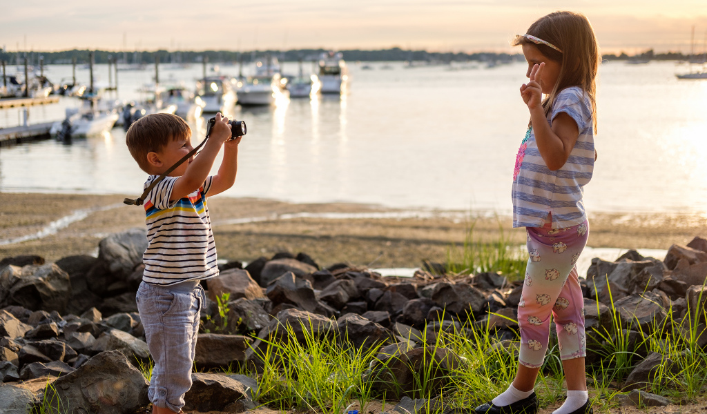 Маленький мальчик фотографирует девочку на берегу