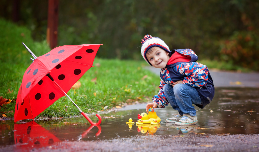 Маленький мальчик пускает резиновую уточку в лужу после дождя