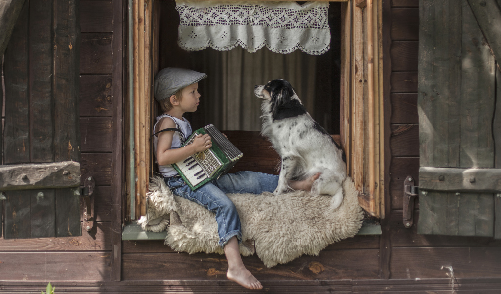 Маленький мальчик с гармошкой сидит на подоконнике с собакой