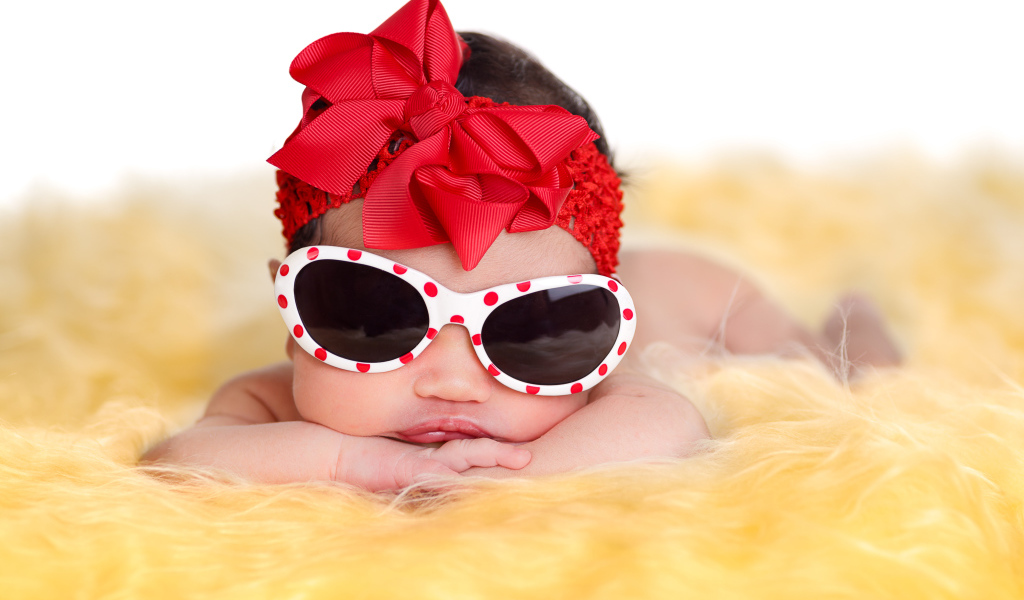 Маленькая забавная малышка в очках и с красным бантом на голове