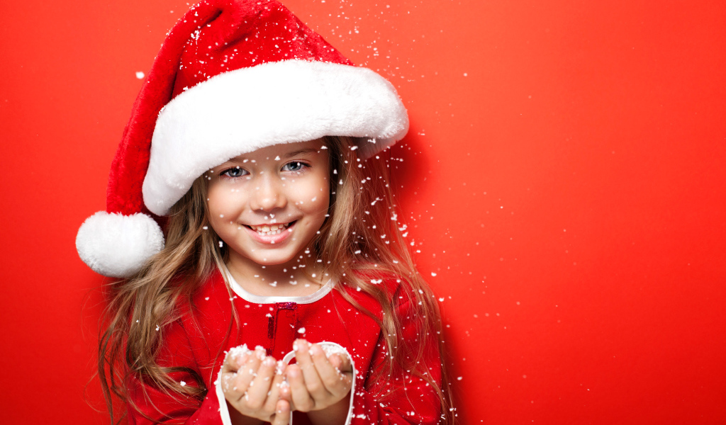 Маленькая девочка в новогодней шапке ловит руками снежинки