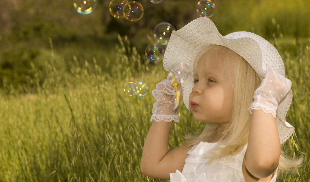 Маленькая девочка в большой белой шляпе пускает мыльные пузыри