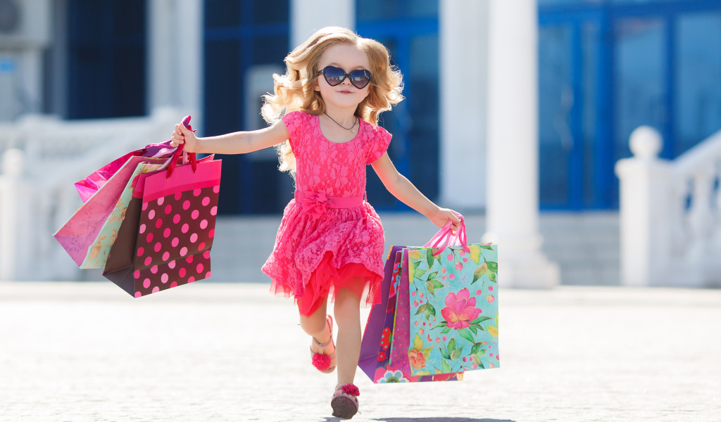 Маленькая девочка в розовом платье бежит с покупками из магазина