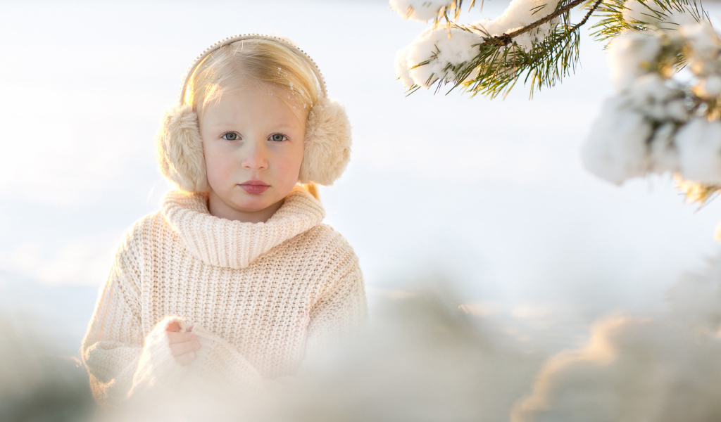 Маленькая девочка в белом свитере у покрытой снегом ели