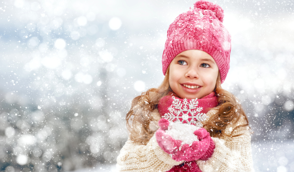 Маленькая девочка в зимней одежде держит снег в руках