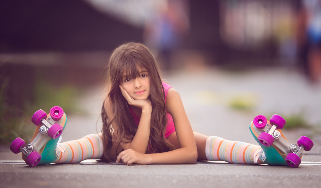 Маленькая девочка сидит на дороге в роликах