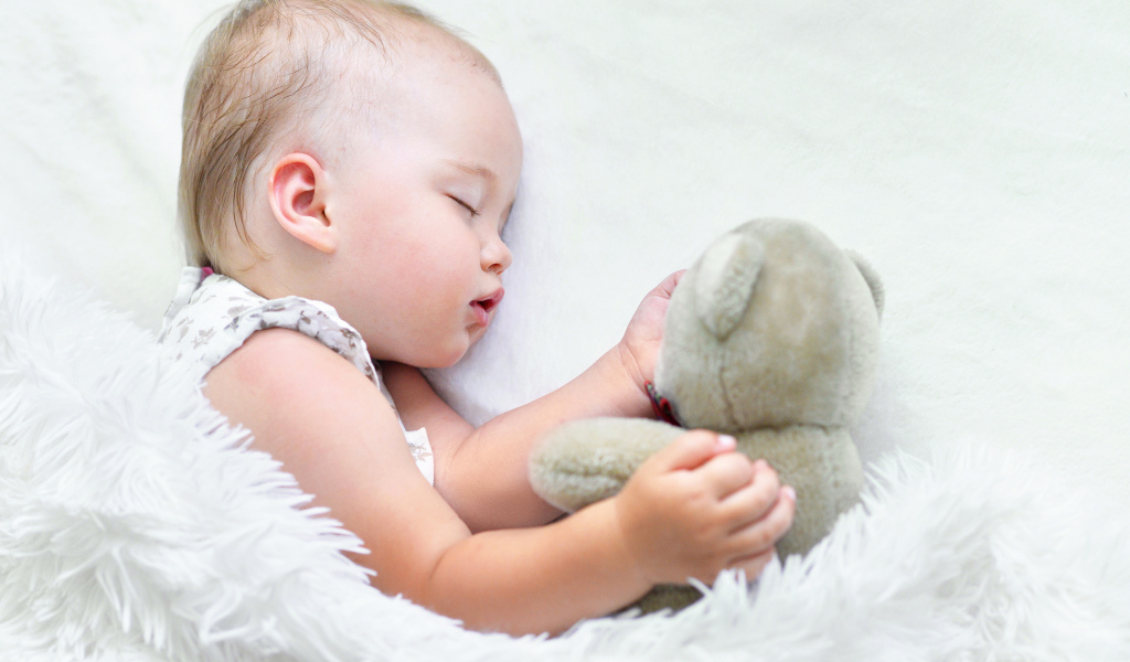 Маленькая девочка спит с мягкой игрушкой под белым одеялом