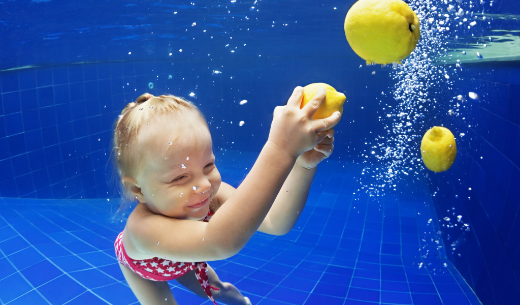 Маленькая девочка плавает в бассейне с желтыми лимонами