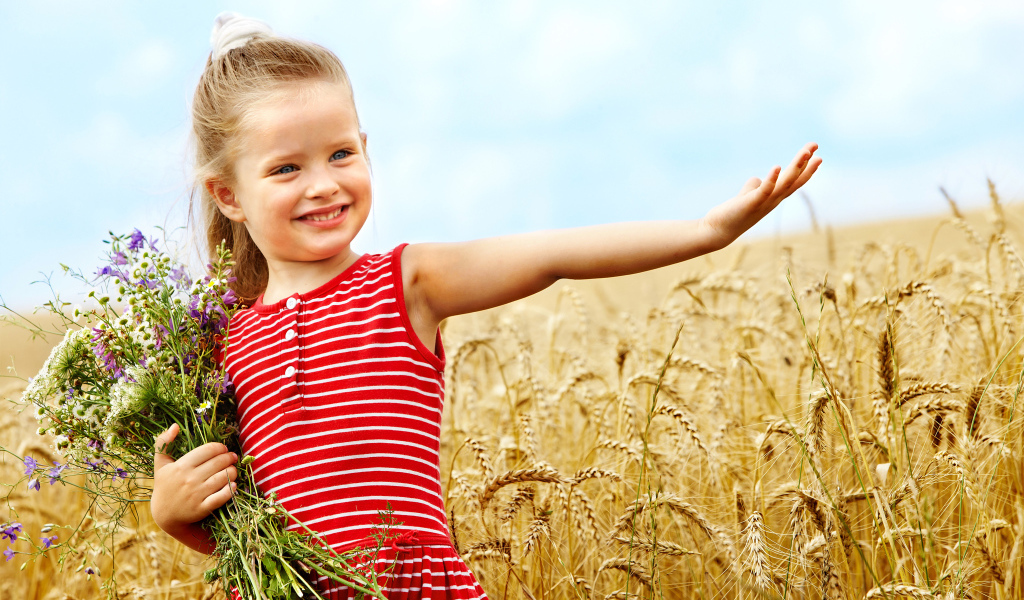 Маленькая девочка с букетом полевых цветов гуляет по полю пшеницы