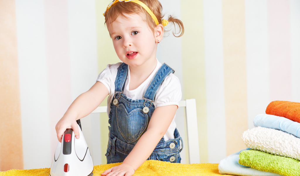 Маленькая девочка с утюгом гладит полотенце