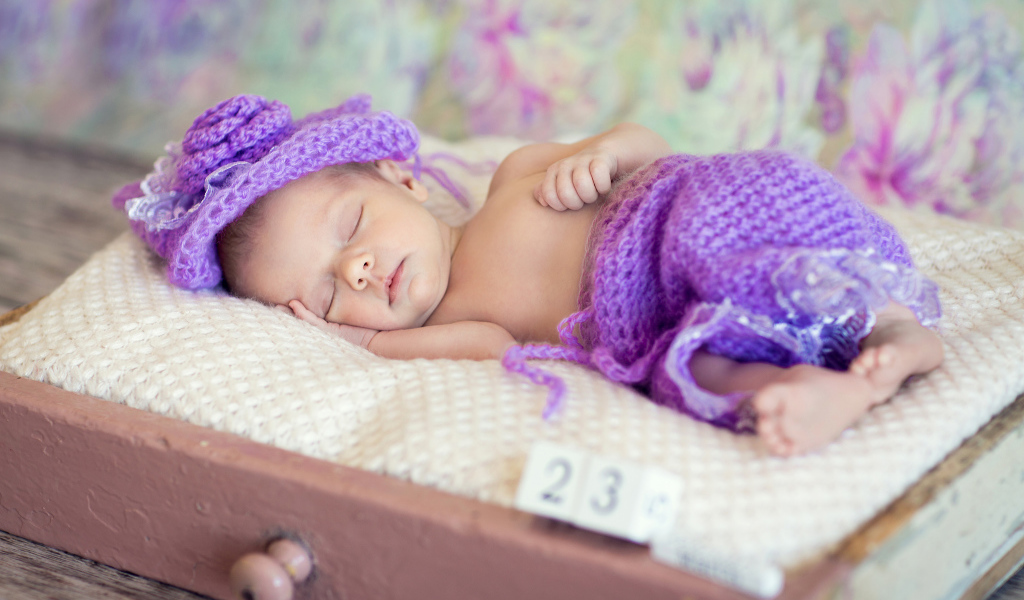 Маленький спящий младенец в вязаном фиолетовом костюме