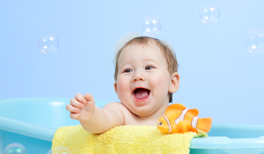 Веселый малыш купается в ванной с игрушечной рыбкой