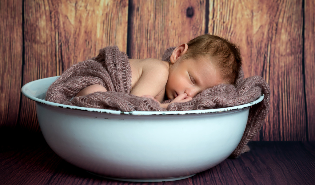Новорожденный ребенок спит в белой миске
