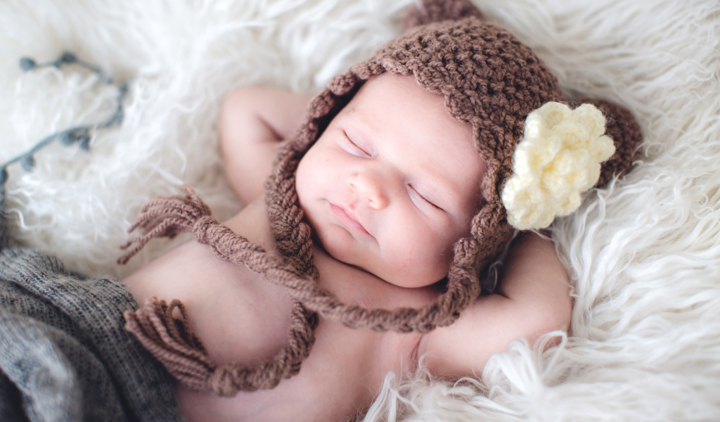 Спящий грудной ребенок в коричневой вязаной шапке с белым цветком