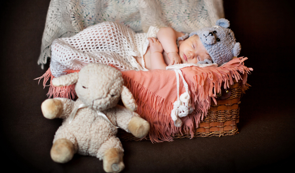 Спящий грудной ребенок в забавной шапке с мягкой игрушкой