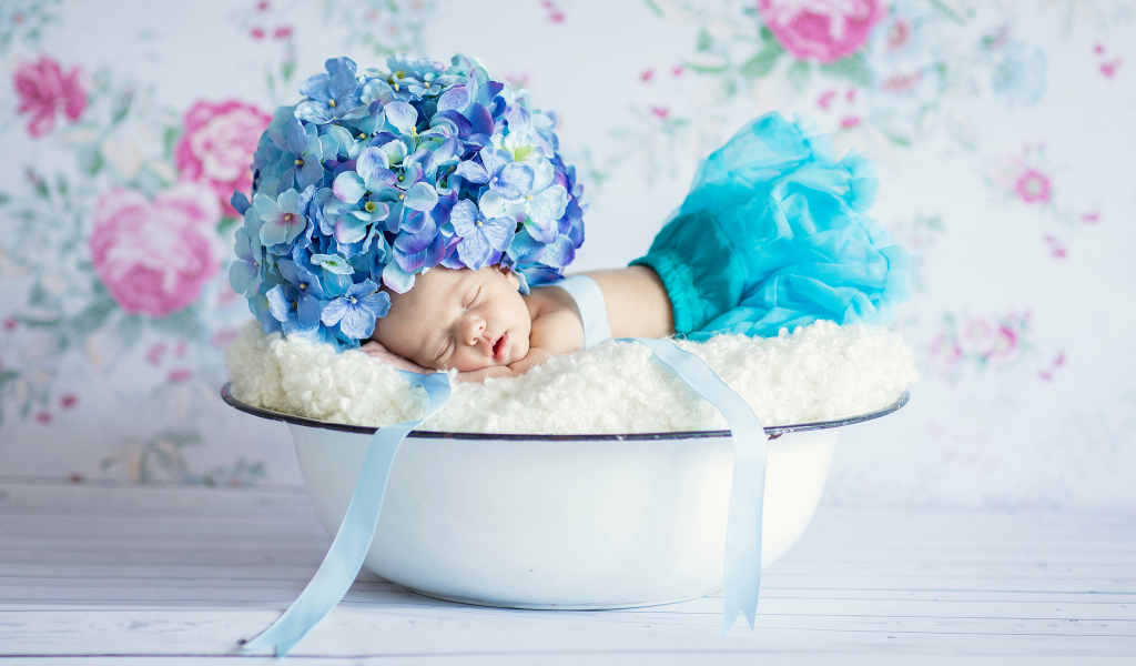 Маленький грудной ребенок спит в миске с шапкой из цветов гортензии на голове