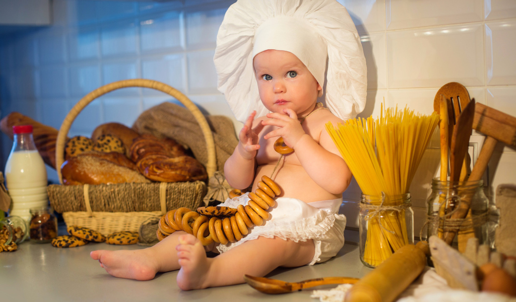 Маленький ребенок в шапке повара сидит на столе с выпечкой