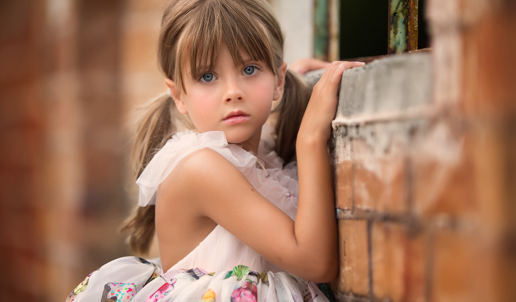 Милая девочка с серьезным взглядом стоит у стены