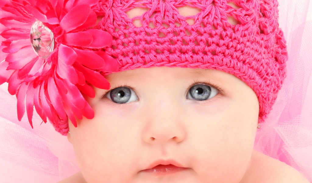 Милая голубоглазая малышка в розовой шапке с цветком герберы
