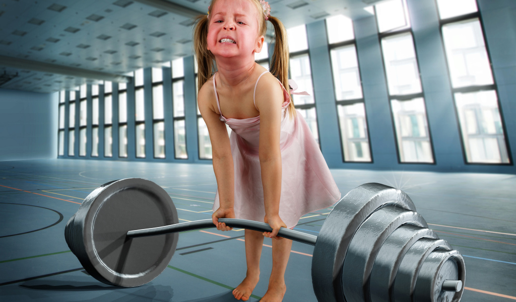 Смешная девочка пытается поднять тяжелую штангу
