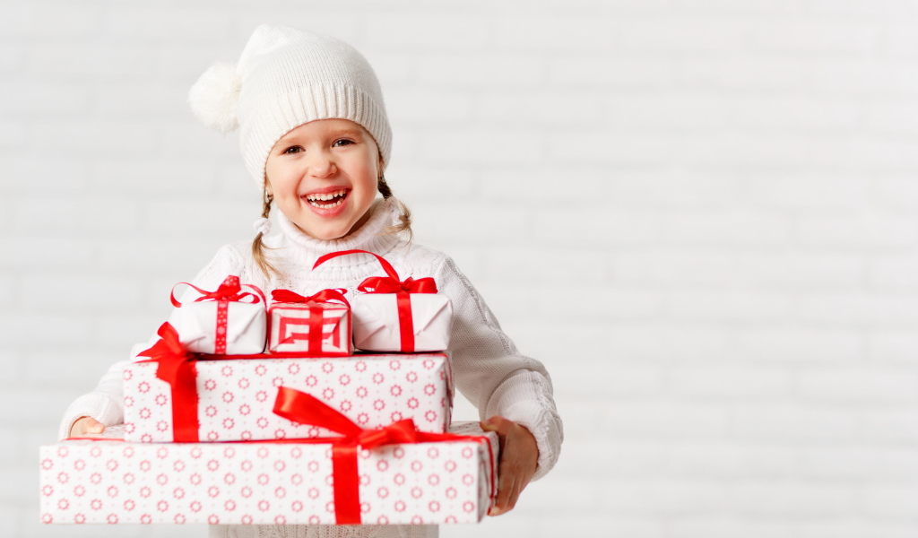 Смеющаяся девочка в белой шапке с новогодними подарками