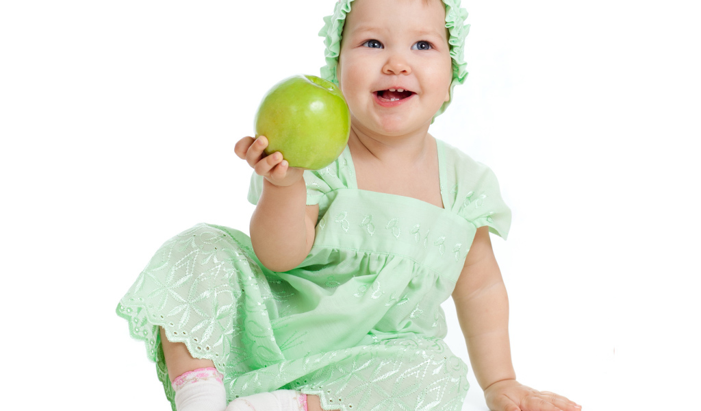 Маленькая голубоглазая девочка с зеленым яблоком в руках