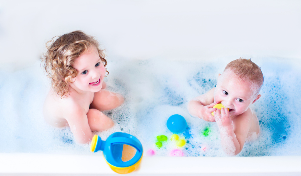 Маленькие мальчик и девочка купаются в ванной с игрушками