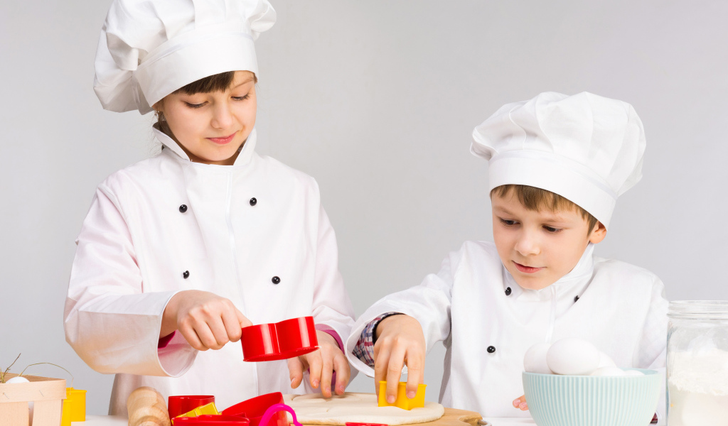 Маленькие мальчик и девочка готовят на кухне печенье